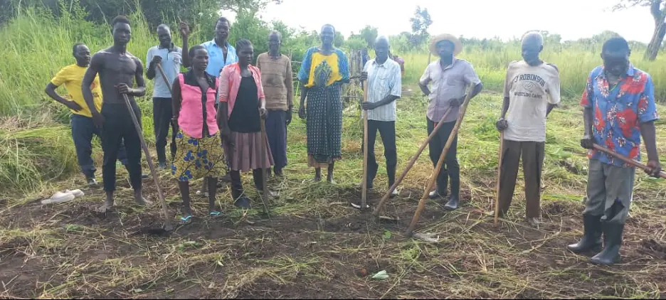 The Kitgum working group standing in a cleared field with hoes