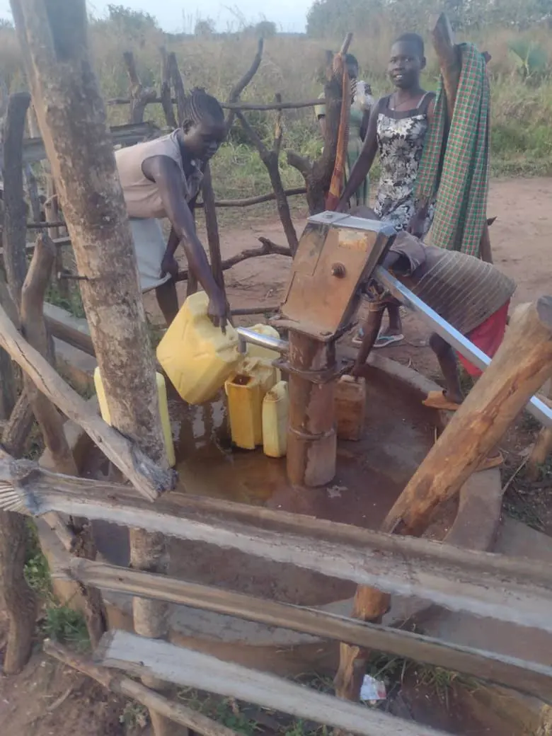 Two women filling yellow jerrycans at the village hand pump well
